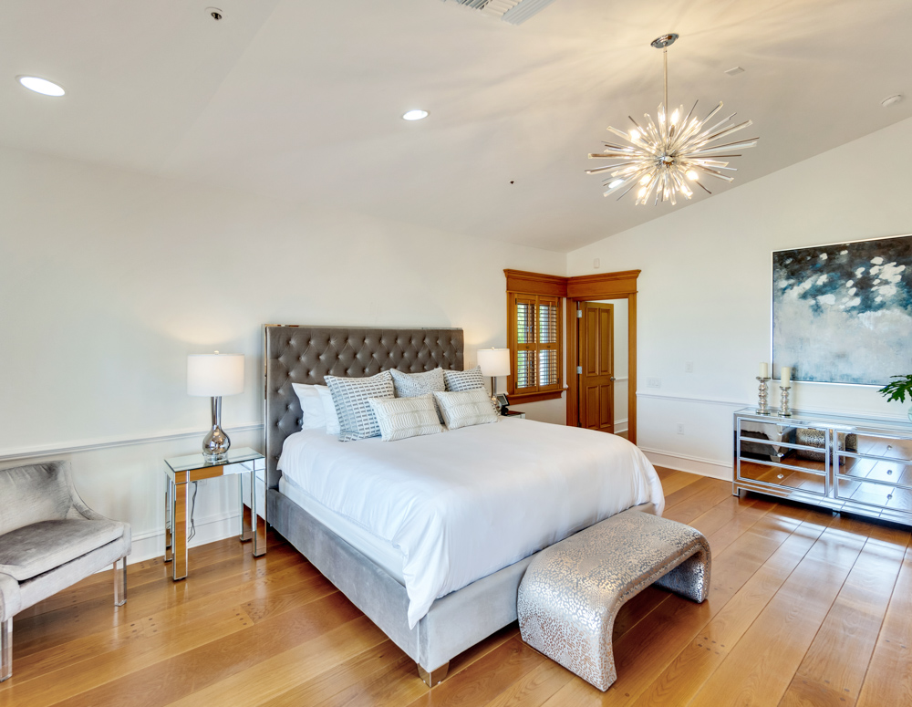 Large bed with white linens and pillows next to silver bed table with lamp and chairs at the Sea Palms Estate in Captiva Island, FL
