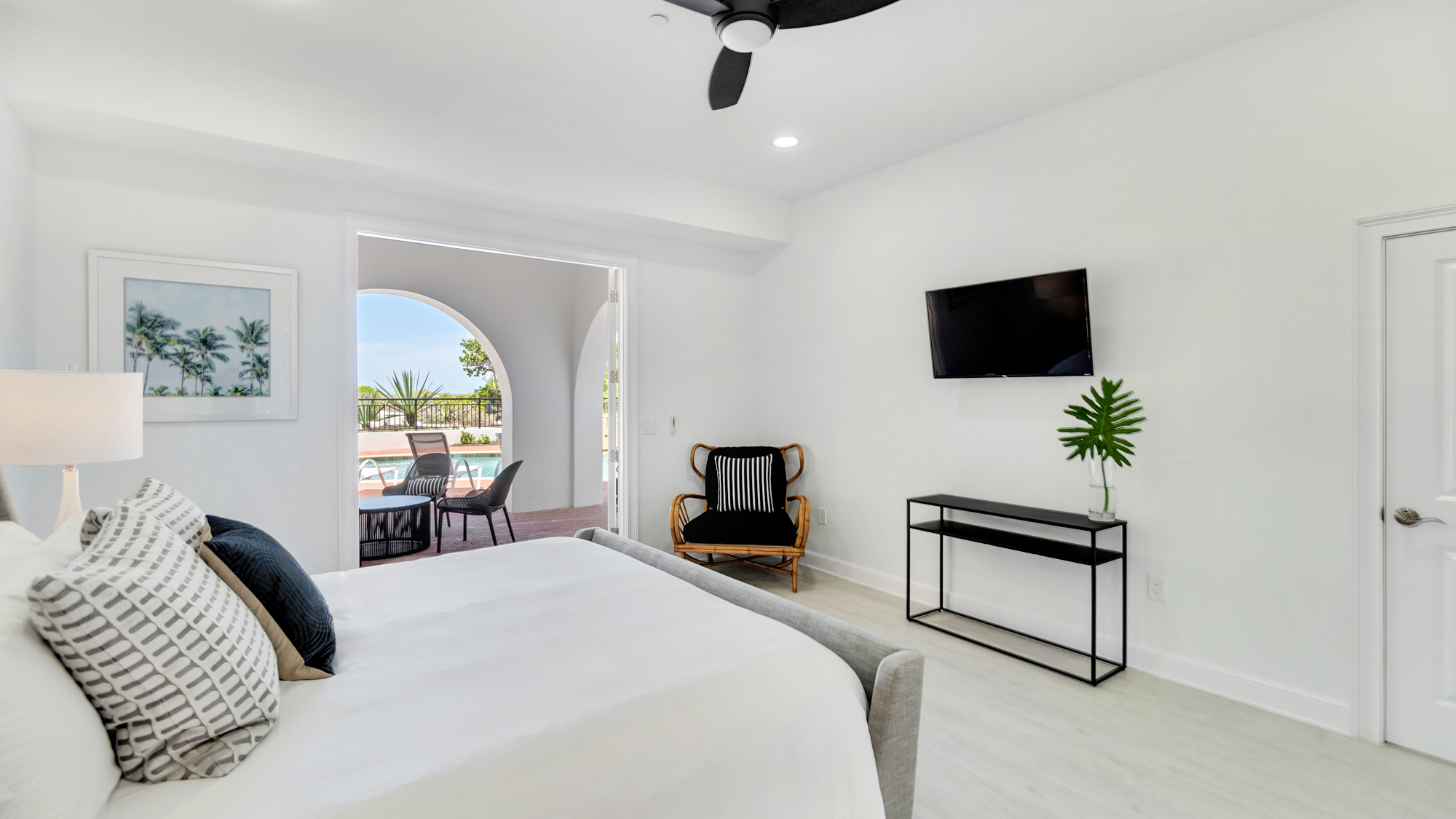 Large bed with white linens and black and white pillows in front of television hanging on the wall over looking pool at the Sea Palms Estate in Captiva Island, FL