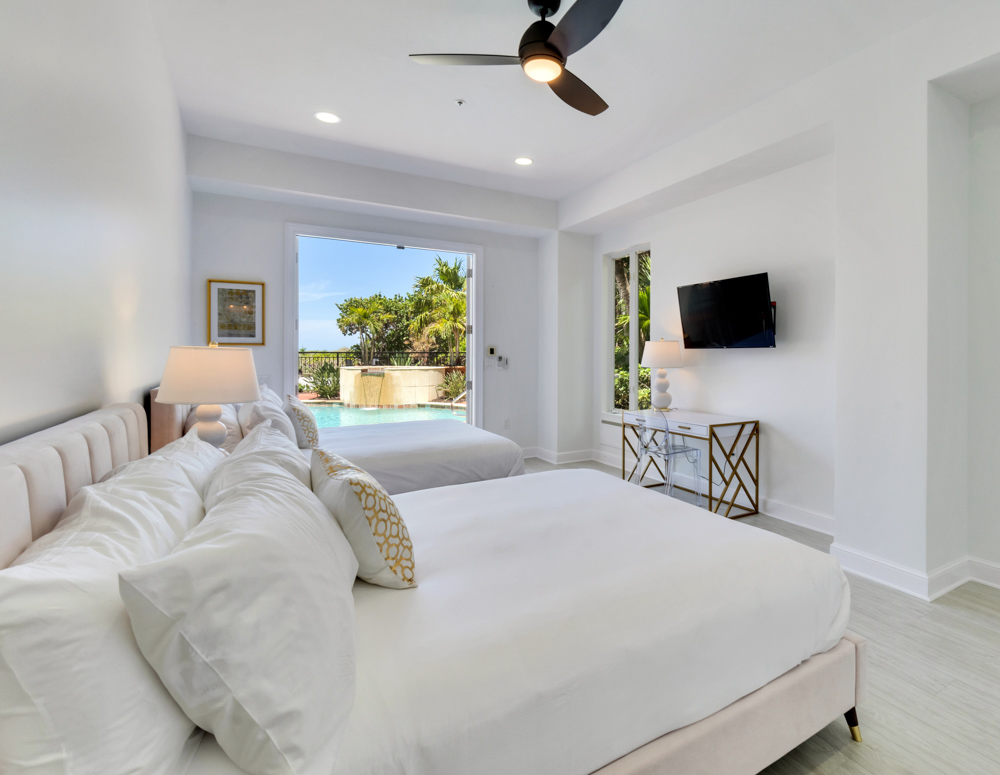 Two large beds with white linens and pillows in front of hanging television overlooking pool at the Sea Palms Estate in Captiva Island, FL