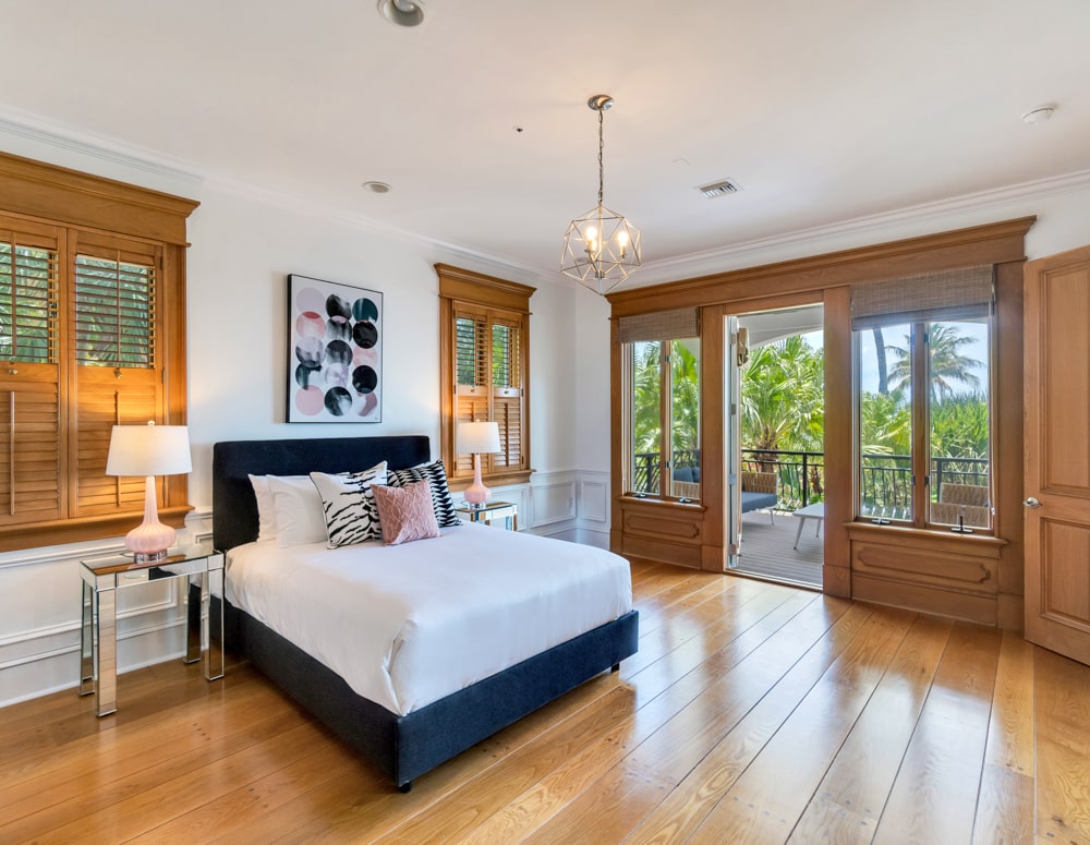 Large bed with white linens and colorful pillows near lamps on bedside table overlooking porch and palm trees at the Sea Palms Estate in Captiva Island, FL